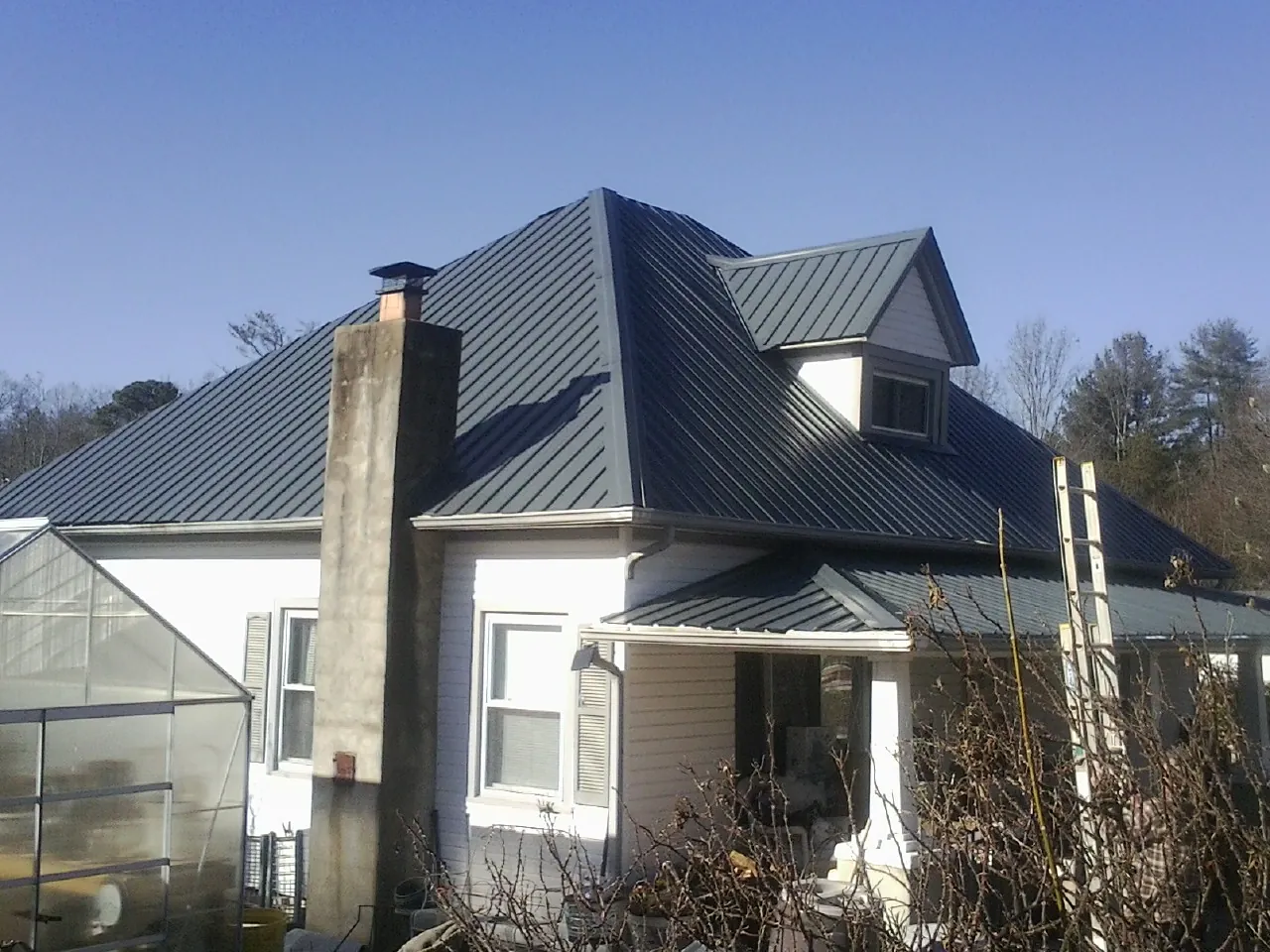 Dark blue standing seam metal roof on a white farmhouse with dormer — Slate & Tile Roof Repair by Roofing Brothers in Hope Mills