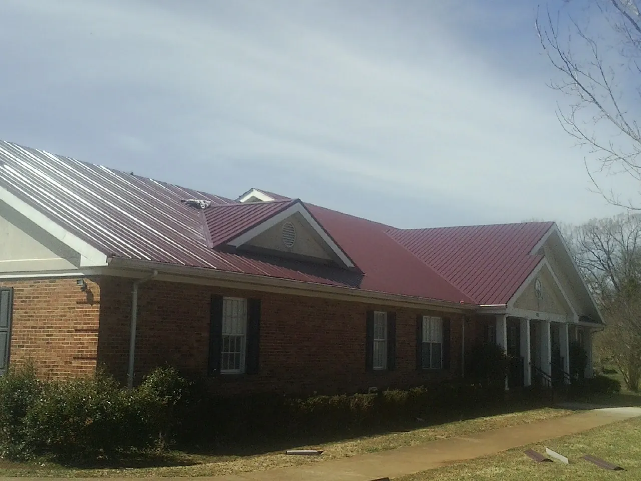 Red metal roof with gabled entries on a long brick building, from a Hail Damage Roof Repair job in Hope Mills