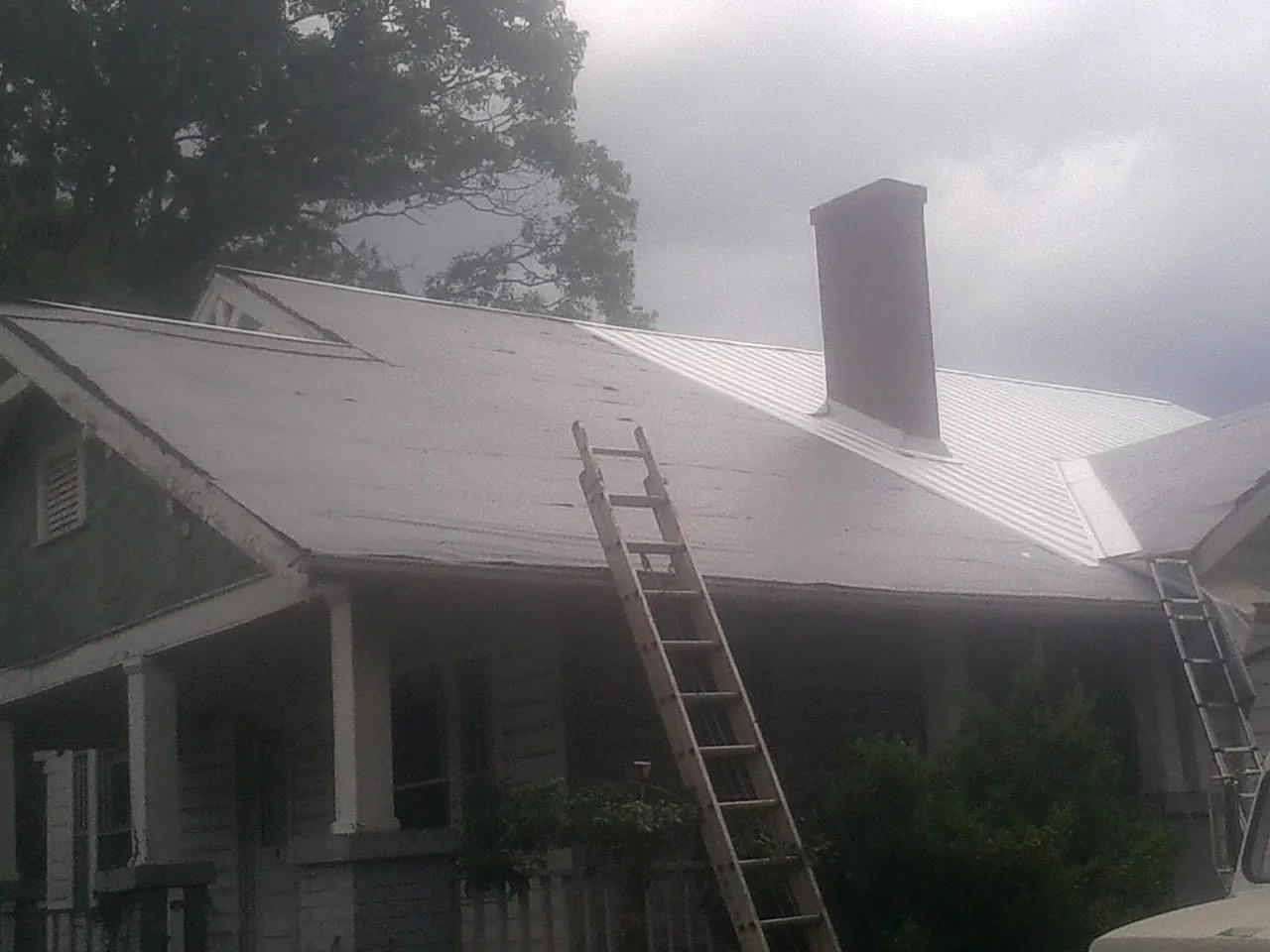 Ladders against a metal roof on an older home with a brick chimney in Hope Mills