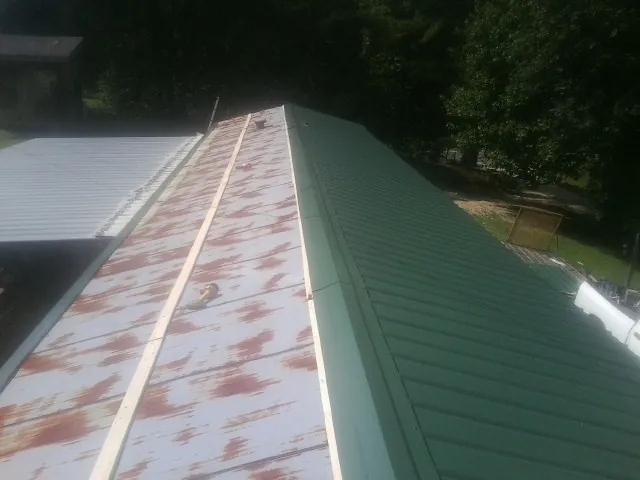 Old rusted panels beside newly installed green metal roofing — Wind Damage Roof Repair by Roofing Brothers in Hope Mills
