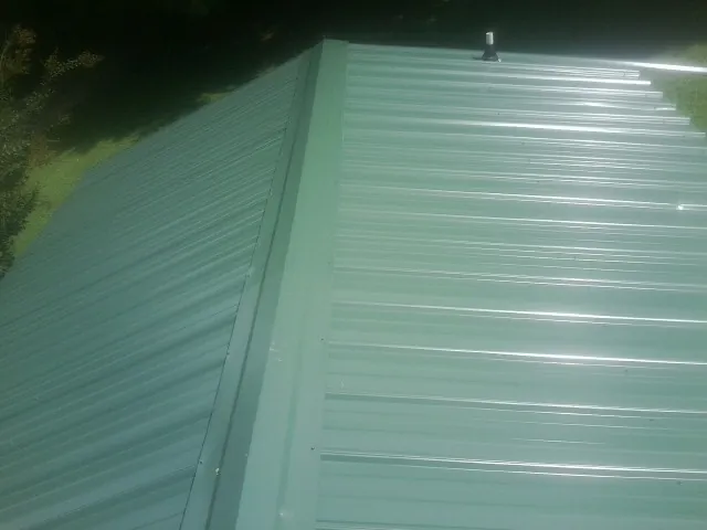 New green metal panels meeting at the ridge of a roof — Flat Roof Repair work by our crew in Hope Mills