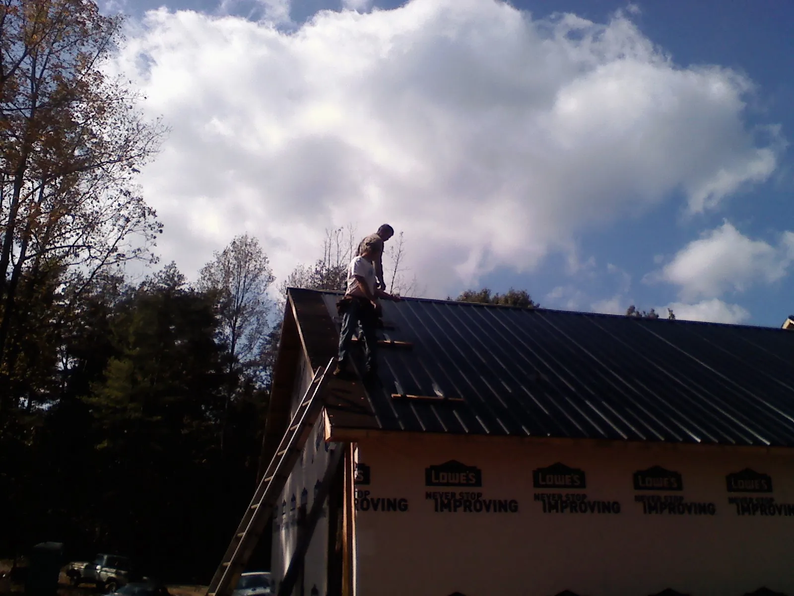 Roofer fastening dark metal panels high against a cloudy sky, from a Roof Inspection job in Hope Mills