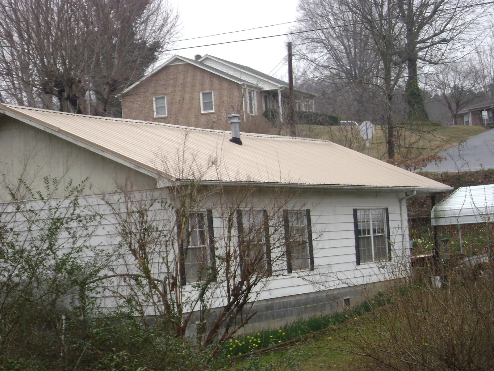 Tan metal roof on a white sided house set into a hillside — Commercial Roofing by Roofing Brothers in Hope Mills