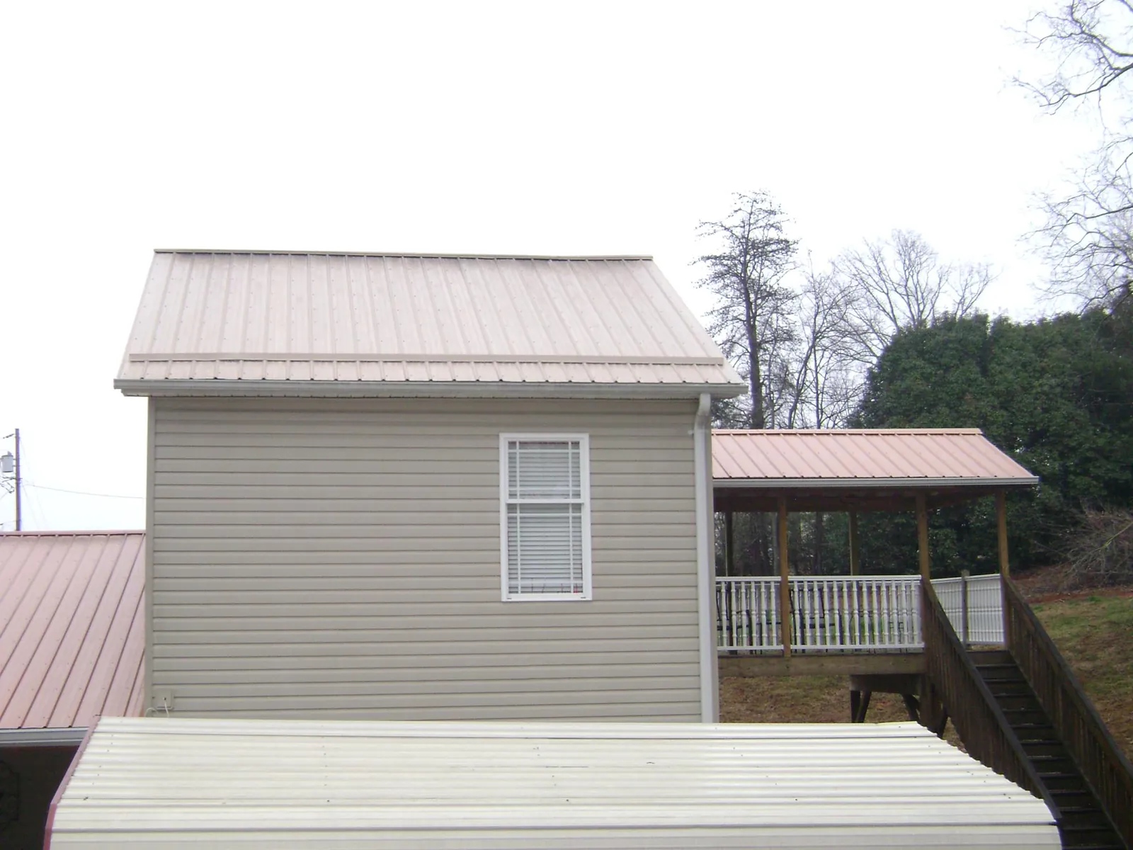 Tan metal roofs on a two story addition and attached porch, from a Roof Replacement job in Hope Mills
